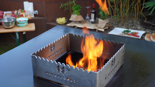 FyrR Cortenstahl Feuerplattengrill mit Fleisch auf der Grillfläche über offenem Feuer